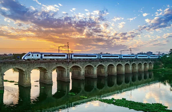 India's indigenously developed semi high speed train crossing bridge with nice evening sky and reflection in water.
