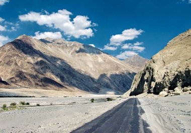 Dağlar ve akan Shyok nehri mavi gökyüzü arka planında beyaz bulutlarla Nubra Vadisi 'ndeki Diskit' e gidiyor, Leh..