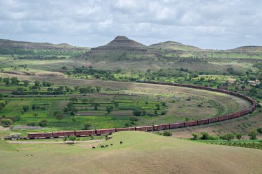 Daundaj, Maharashtra, Hindistan 'da muson bulutları havada süzülürken, tepe demiryolu hattında büyük bir virajdan geçen uzun yük treni..