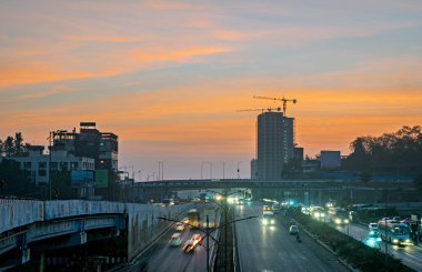 Gün doğumu zamanı, ışık yollarının yavaş çekim hızı, güzel gökyüzü, binalar ve yeni geliştirilen otoyol kavşağında akan trafik.