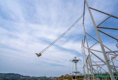 Mavi gökyüzünün altındaki bir uçurumun yanında büyük bir salıncak.