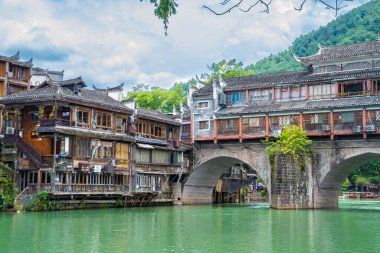 Görüntü Fenghuang Antik Kenti, Xiangxi, Hunan 'daki nehrin kenarındaki geleneksel Miao köyü mimarisini gösteriyor. Yeşil su ve mavi gökyüzü muhteşem bir manzara yaratıyor.