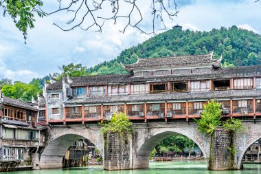 Görüntü Fenghuang Antik Kenti, Xiangxi, Hunan 'daki nehrin kenarındaki geleneksel Miao köyü mimarisini gösteriyor. Yeşil su ve mavi gökyüzü muhteşem bir manzara yaratıyor.