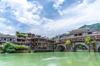 Görüntü Fenghuang Antik Kenti, Xiangxi, Hunan 'daki nehrin kenarındaki geleneksel Miao köyü mimarisini gösteriyor. Yeşil su ve mavi gökyüzü muhteşem bir manzara yaratıyor.