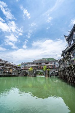 Görüntü Fenghuang Antik Kenti, Xiangxi, Hunan 'daki nehrin kenarındaki geleneksel Miao köyü mimarisini gösteriyor. Yeşil su ve mavi gökyüzü muhteşem bir manzara yaratıyor.