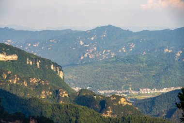 Zhangjiajie 'deki kaya sütunlarını ve dağları sis kaplıyor, vadide güneş ışığı var.