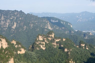 Zhangjiajie 'deki kaya sütunlarını ve dağları sis kaplıyor, vadide güneş ışığı var.