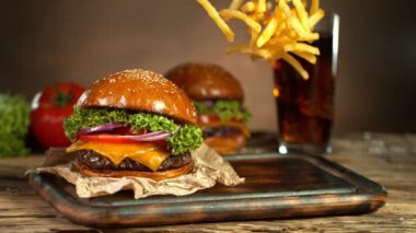 Fast Food Concept 'ın Süper Yavaş Çekimi. Taze Hamburger 'in yanındaki tahta kesme tahtasına patates kızartması düşüyor. 4K 'da Yüksek Hız Sinema Kamerası ile çekildi..