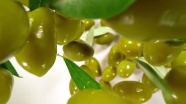 Düşen Taze Yeşil Zeytinlerin Süper Yavaş Çekimi ve Beyaz Arkaplanda Yapraklar 1000 fps. Yüksek Hız Sinema Kamerası ile 4K çözünürlükte çekilmiştir.