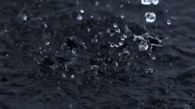 Super Slow Motion Shot of Water Drops Falling and Splashing into Water on Black Background at 1000 fps. Filmed with High Speed Cinema Camera in 4K Resolution.