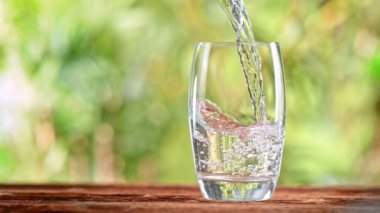 Super Slow Motion Shot of Pouring Pure Water into Glass on Green Natural Background at 1000fps. Filmed with High Speed Cinema Camera in 4k.