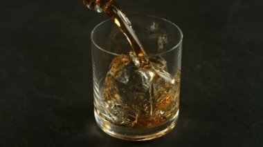 Super Slow Motion Shot of Pouring Whiskey into Glass with Ice Cube at 1000fps with Camera Movement. Filmed with High Speed Cinema Camera at 4K.