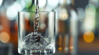 Super Slow Motion Detail Shot of Pouring Transparent Alcohol Liquid into Glass with Ice on Bar at 1000fps. Filmed with High Speed Cinema Camera, 4K.