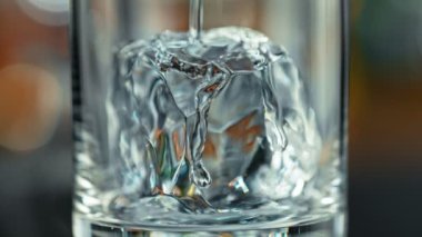 Super Slow Motion Detail Shot of Pouring Transparent Alcohol Liquid into Glass with Ice on Bar at 1000fps. Filmed with High Speed Cinema Camera, 4K.