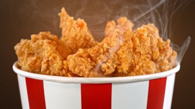 Slow Motion shot of Fried Chicken Pieces ve Smoke Rotting in a Bucket on Brown Background. Yüksek Hız Sinema Kamerası, 4K.