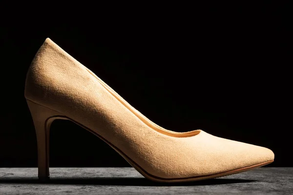 Side view of a beige womens shoe with a heel on a dark background.