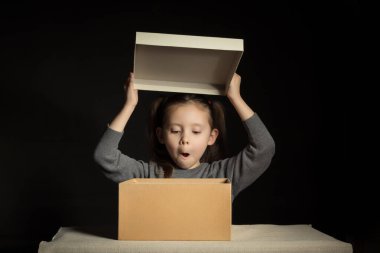 Emotional little girl opens a long-awaited package with a gift, copy space on cardboard box.
