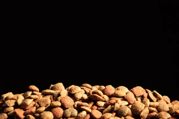 Close-up of dry dog food in warm colors on a black background.