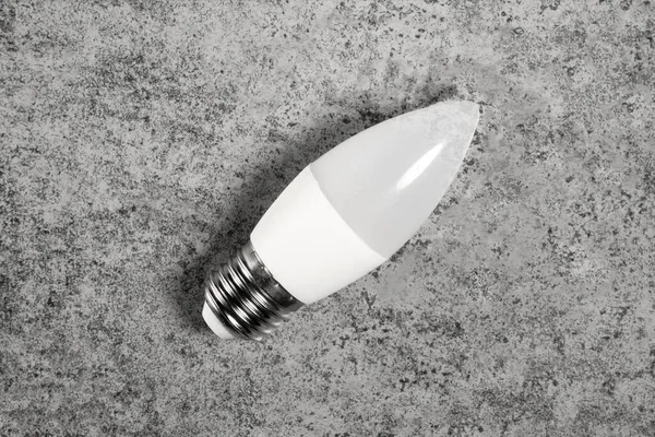 LED energy-saving lamp with E27 screw cap base in form of candle, on gray background.