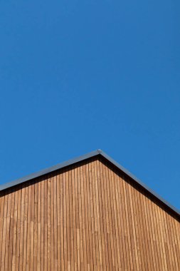 Rooftop with wooden plank gable on new modern home against clear blue sky.
