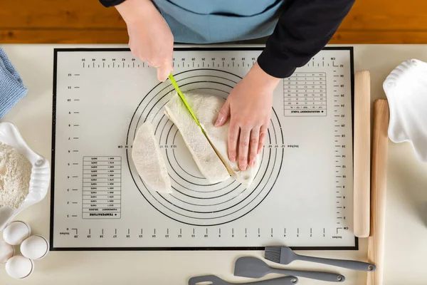 Cutting dough on a silicone baking mat with a special plastic knife, top view.