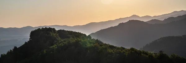 Panorama with layered summer mountains in the morning haze at sunset in central Asia.