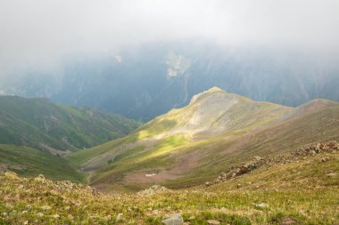Mysterious minimalist high-altitude picturesque mountain landscape with clouds touching large peaks in Almaty mountains of Kazakhstan nature.