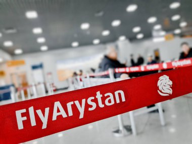 Uluslararası havaalanında ziyaretçilerle bekleme odasında Fly Arystan logosu olan bariyer bandı. Almaty, Kazakistan - 23 Aralık 2022.