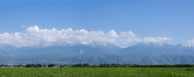 Uzakta bulunan Almaty City manzarası karla kaplı Tian Shan dağları ve bulutlu gökyüzü. Almaty, Kazakistan - 26 Mayıs 2022