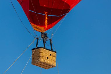 Açık mavi gökyüzüne karşı kırmızı bir balondan boş bir sepet.