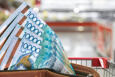 Kazakistan 'da gıda ürünlerinin fiyatları yükseliyor. Bulanık bir marketin arka planında cüzdanda bir tenge.