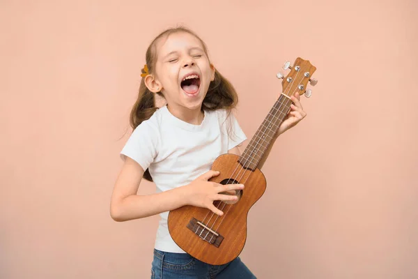 Expressive emotional caucasian girl of primary school age sings along with herself on the ukulele.