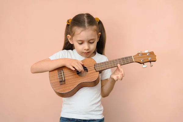 Preschool girl learning music by playing ukulele.
