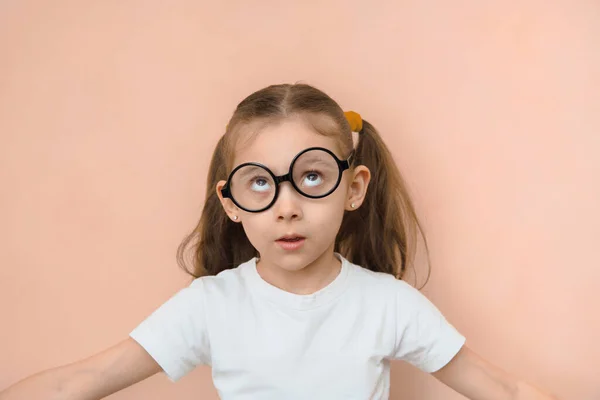 Confused funny little girl of primary school age with crooked round glasses.