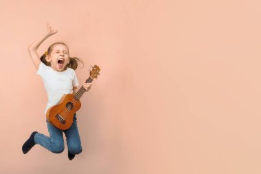Pembe arka planda rock yıldızı gibi ukulele çalan duygusal küçük atlayan kız, boşluğu kopyala.