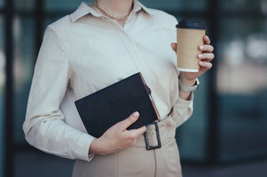 Notlar için bir deftere yakın çekim ve bir ofis çalışanının elinde kahve olan bir kağıt bardak..