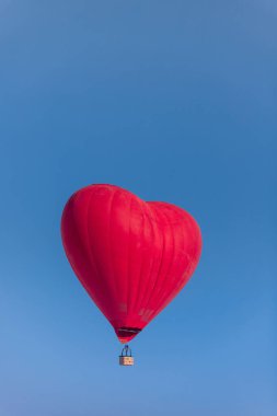 Açık mavi gökyüzüne karşı kırmızı kalp şeklinde sıcak hava balonu, balayındaki aşıkların yolculuğu, fotokopi alanı, dikey.