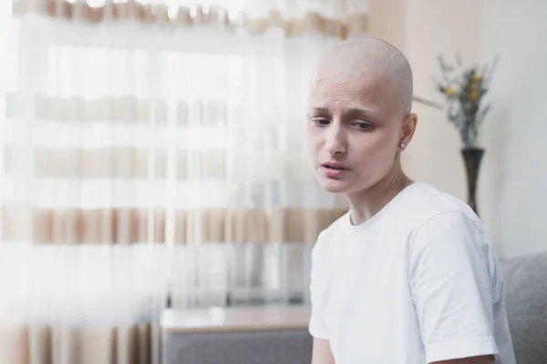 Sad tired bald young woman with oncology in home room after chemotherapy course.