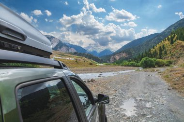 Nehir, dağlar ve Kazakistan 'dan gelen bulutlu gökyüzü karşısında yeşil 4x4 off-road aracıyla seyahat kavramı.