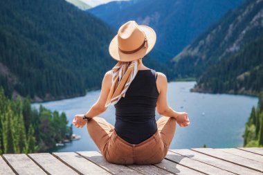 Kazakistan dağlarındaki Kolsai Gölü yakınlarında doğayla uyum içinde olan genç bir kadın. Orta Asya doğası, yerli turizm, tatil kavramı.