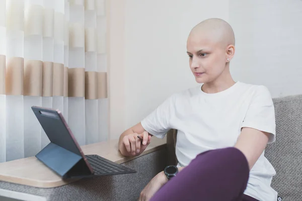 Young bald woman with oncology after chemotherapy is studying remotely at home.