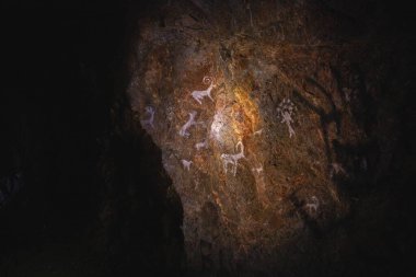 Hayvan figürleri ve Tanrı 'nın görüntüsü mağaranın taş duvarında antik tarih öncesi insanları çiziyor..