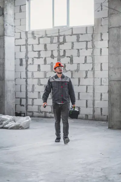 Workman ready for renovation work. Builder in uniform carrying toolbox at construction site, copy space, vertical.