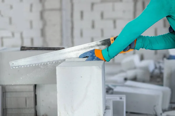 Sawing an autoclaved aerated gas block with a hand saw at a construction site during the construction of internal partitions of a building.