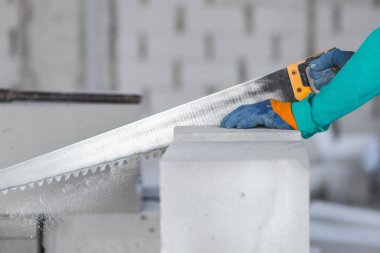 İnşaat alanında çalışan bir işçi, inşaat alanındaki havalandırmalı betondan bir yapı bloğunu kesiyor..