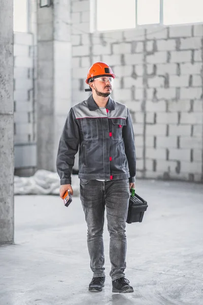 Worker man ready for renovation work in new apartment. Builder in overalls carrying toolbox at construction site, vertical.