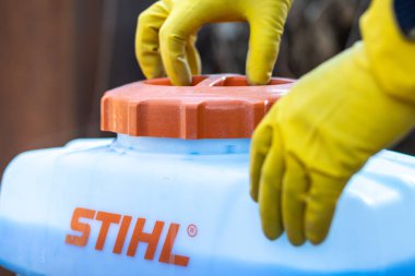 Bahçıvanlar koruyucu eldivenler giyip bir Stihl bahçe spreyinin bakır sülfatıyla kapağını kapatıyorlar. Almaty, Kazakistan - 23 Mart 2023