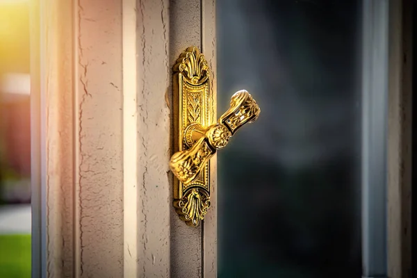 Gold plated door handle on the door with glass inserts with an aged texture on the frame in a luxury interior.