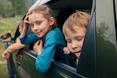 İki neşeli çocuk arabanın penceresinden dışarı bakıp, canlı bir açık hava macerasının tadını çıkarıyorlar.