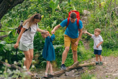Mutlu bir aile güneşli bir günde çocuklarıyla güzel, yemyeşil bir ormanda yürüyüş yapar.